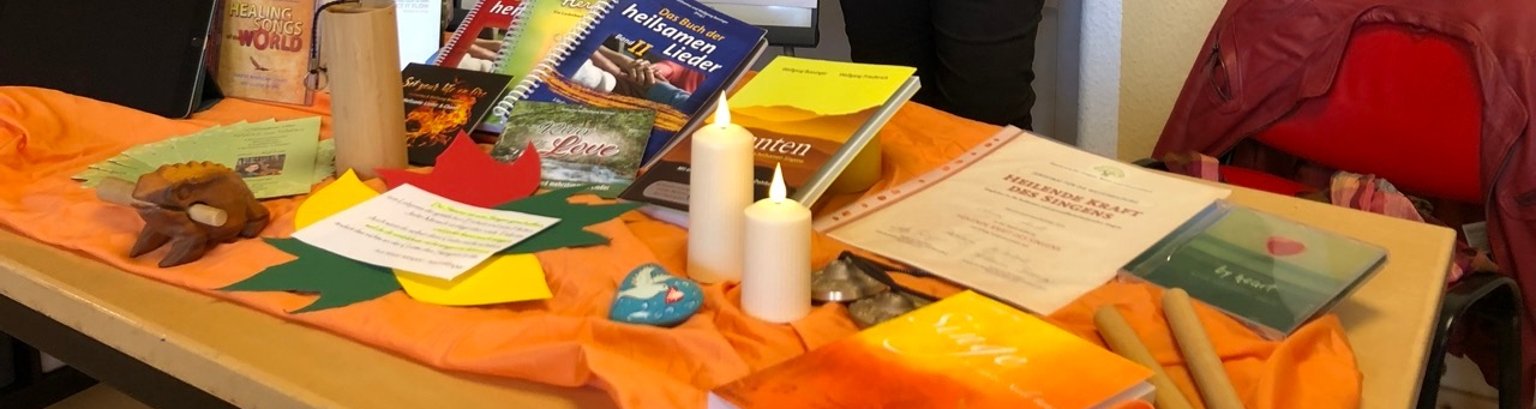 Bildausschnitt: Tisch mit verschiedenen Büchern zum Terme heilsames Singen und zwei brennende Kerzen