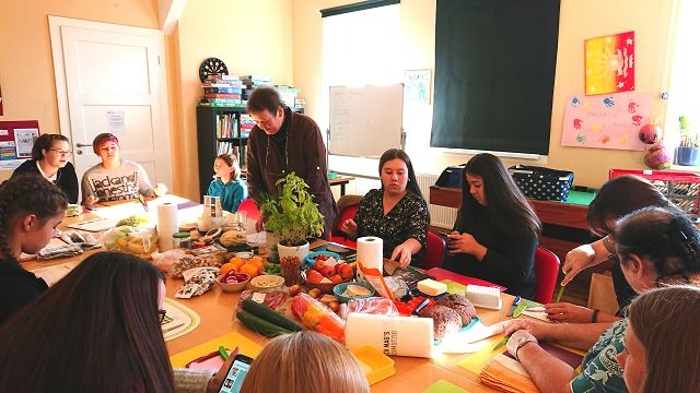 Menschen sitzen um einen Tisch mit Obst und Bastelmaterial und basteln