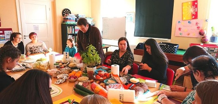 Menschen sitzen um einen Tisch mit Obst und Bastelmaterial und basteln