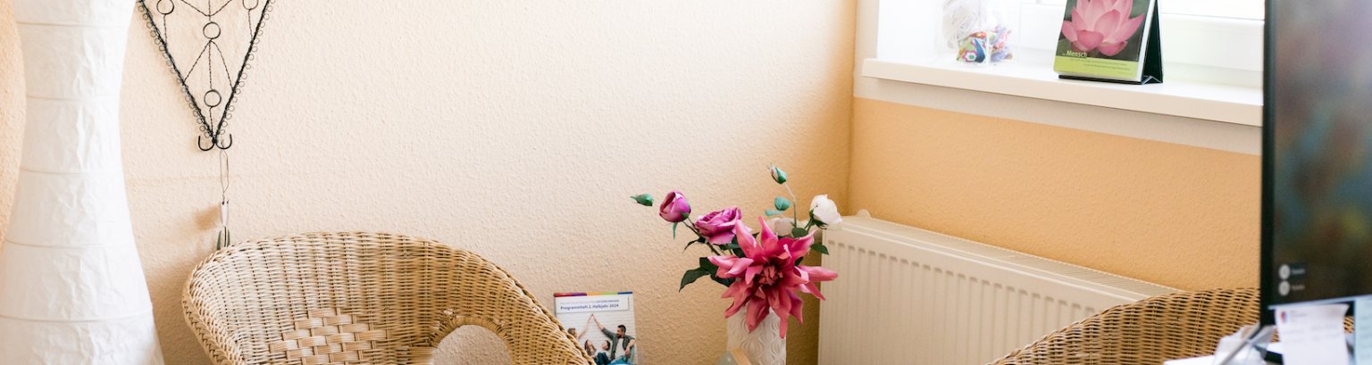 Info-Zeit Junge Familie Bildausschnitt: Teile von zwei Rattan-Stühlen vor einer Wand. Dazwischen eine Vase mit rosa und weißen Schnittblumen.