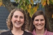 Auf dem Bild sind die Köpfe zweier lächelnder Frauen, eine mit blonden Locken eine mit braunem längerem Haar.
