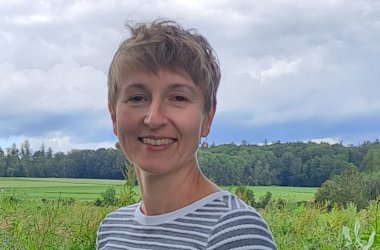 Der Kopf einer blonden Frau vor eine grünen Landschaft und blauem Himmel