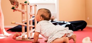 Ein Kleinkind sieht den Murmeln in einer Holzmurmelbahn zu.